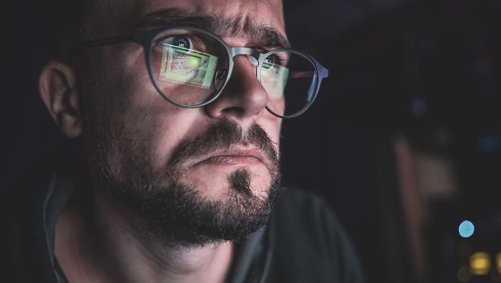 A man with glasses stares intently at a computer screen with a search intent after inserting a keyword