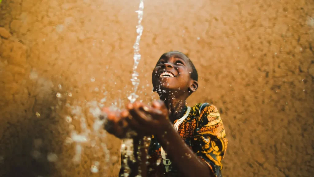 A boy of dark skin receiving water from above
